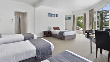 A hotel room with two beds, a desk, and a chair. There is a large window with curtains, and a door leading to another room.