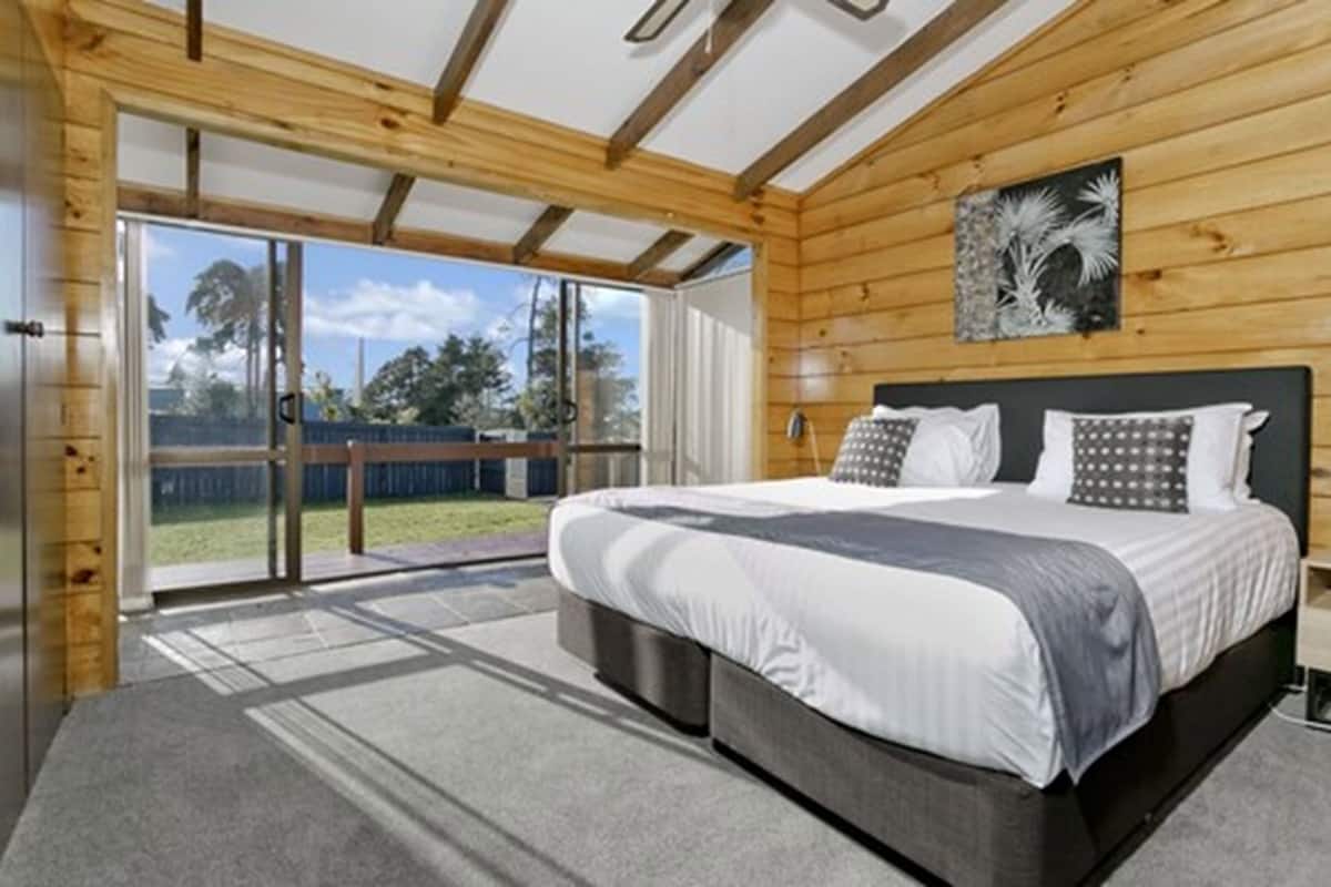 Un dormitorio con una cama grande, paredes de madera, una puerta corrediza de vidrio a un balcón y un cuadro enmarcado en la pared.