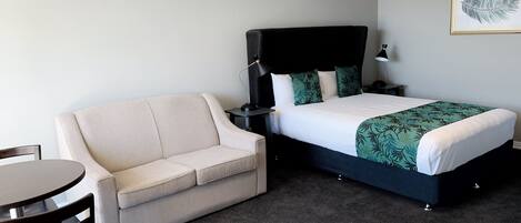 Una habitación de hotel con cama, sofá, una mesita y una silla.