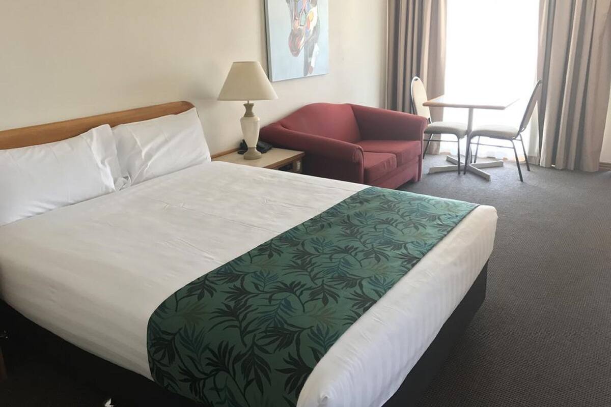 A hotel room with a large bed, a red armchair, a small table, and a lamp.