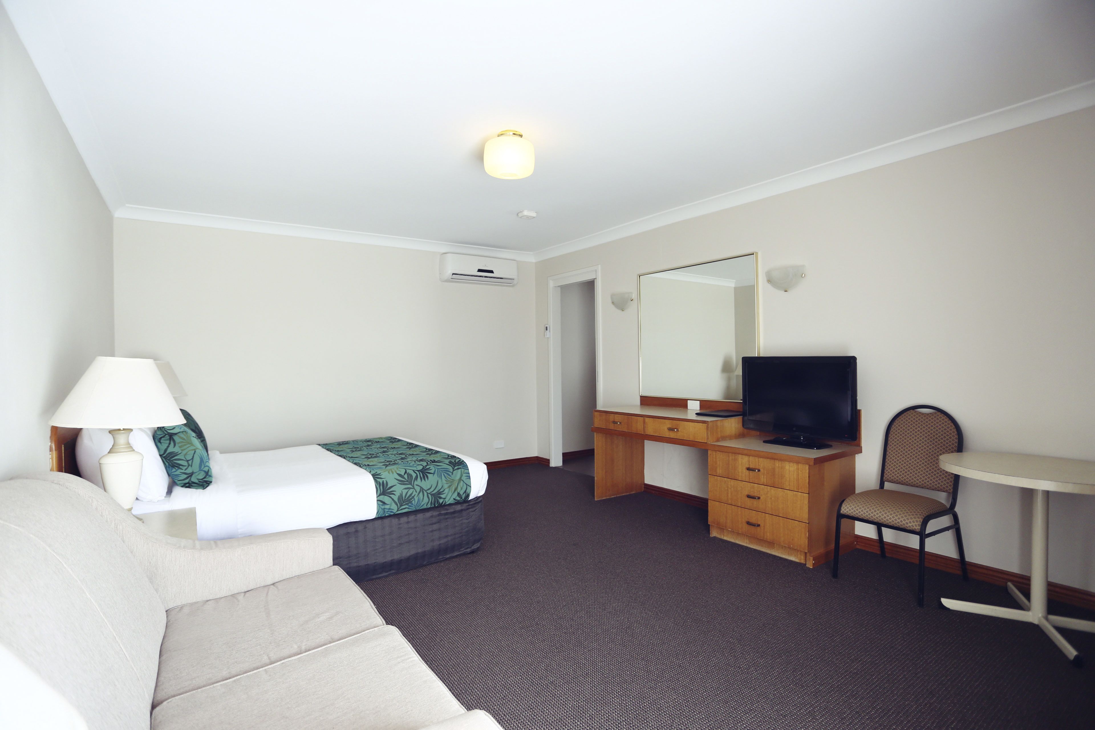 A hotel room with a bed, a desk with a television, a chair, and a lamp.