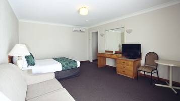 A hotel room with a bed, a desk with a television, a chair, and a lamp.