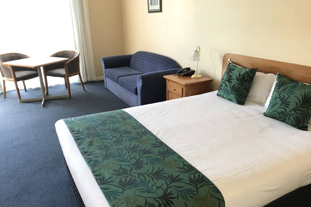 A hotel room with a large bed, a desk with two chairs, a small table with a lamp, and a nightstand with a phone.