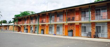 Un motel avec une série de chambres, chacune dotée d’un balcon et d’un petit espace extérieur aménagé pour s’asseoir.