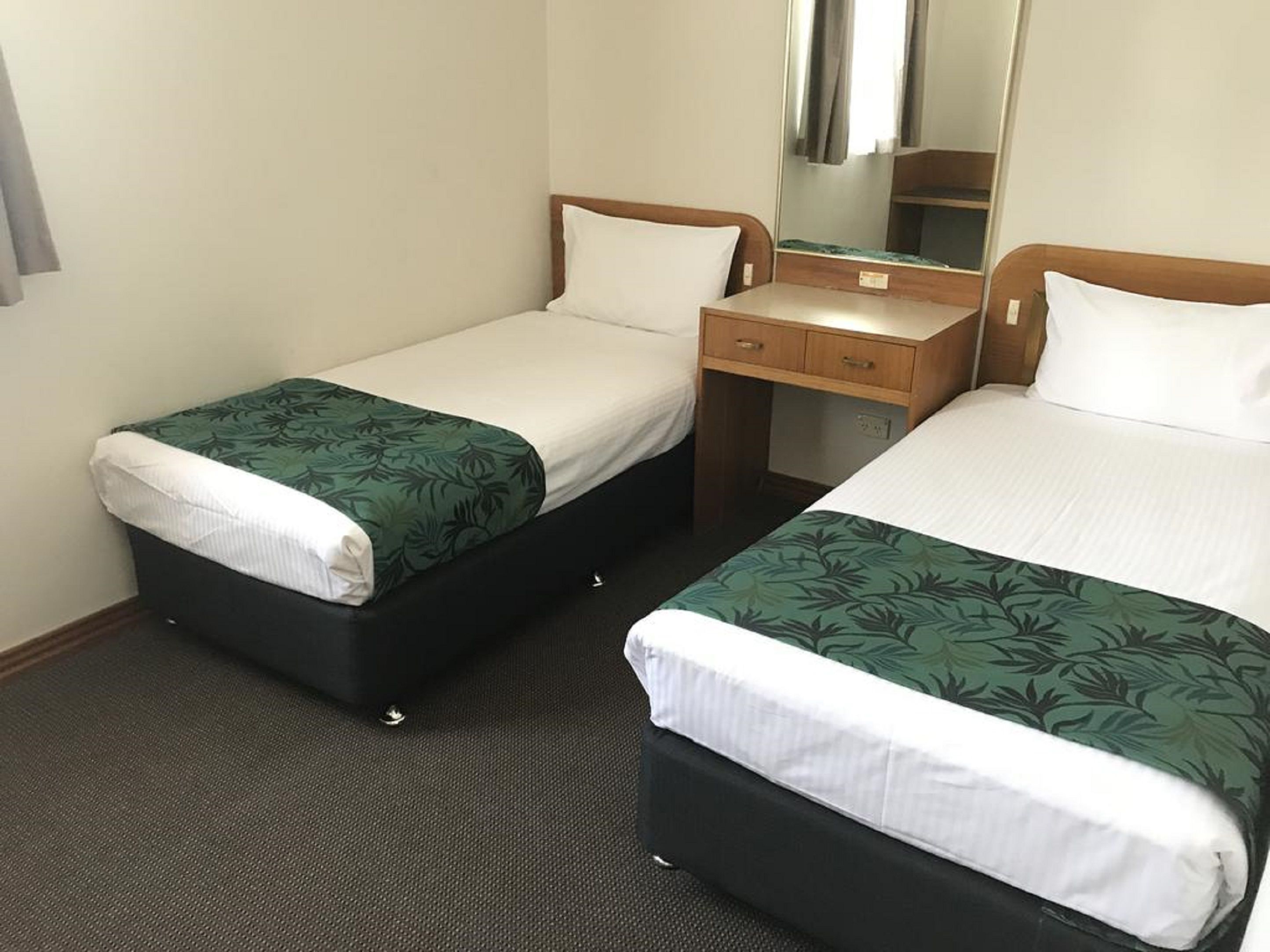 Een hotelkamer met twee enkele bedden, een houten nachtkastje, een spiegel en een vloerbedekking.