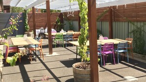 An outdoor patio area with a pergola, tables, chairs, and potted plants. - Cascades Motor Inn  (Dubbo)