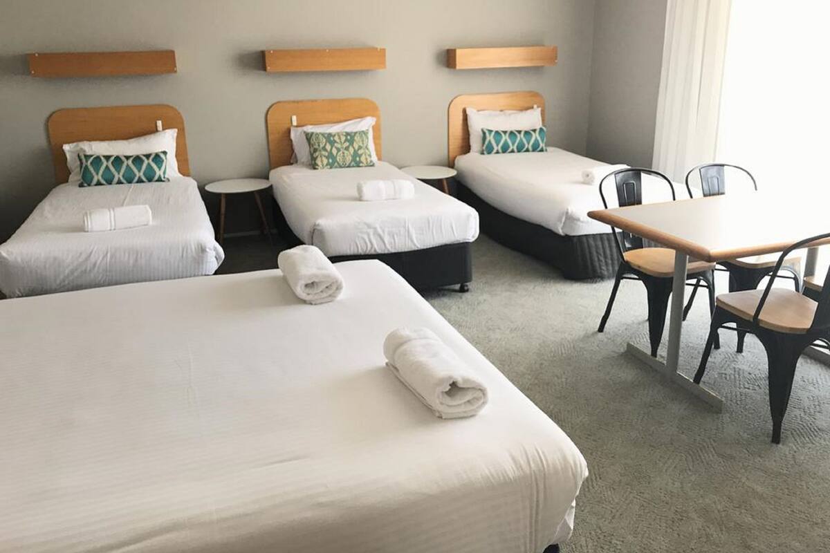 A hotel room with three single beds, a small round table, and two chairs.