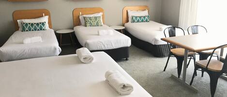 A hotel room with three single beds, a small round table, and two chairs.