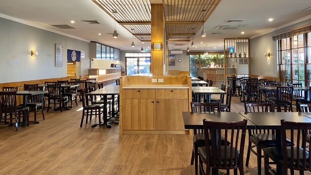 A spacious restaurant interior with wooden tables and chairs, a central counter, and large windows allowing natural light. - Cascades Motor Inn  (Dubbo)