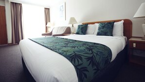 A hotel room with a large bed, a chair, a desk, and a lamp. - Cascades Motor Inn  (Dubbo)