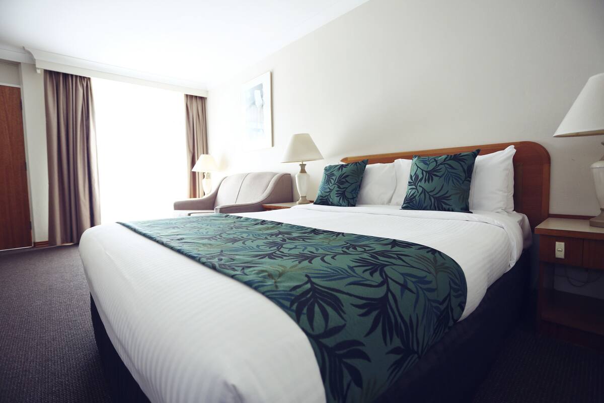A hotel room with a large bed, a chair, a desk, and a lamp.