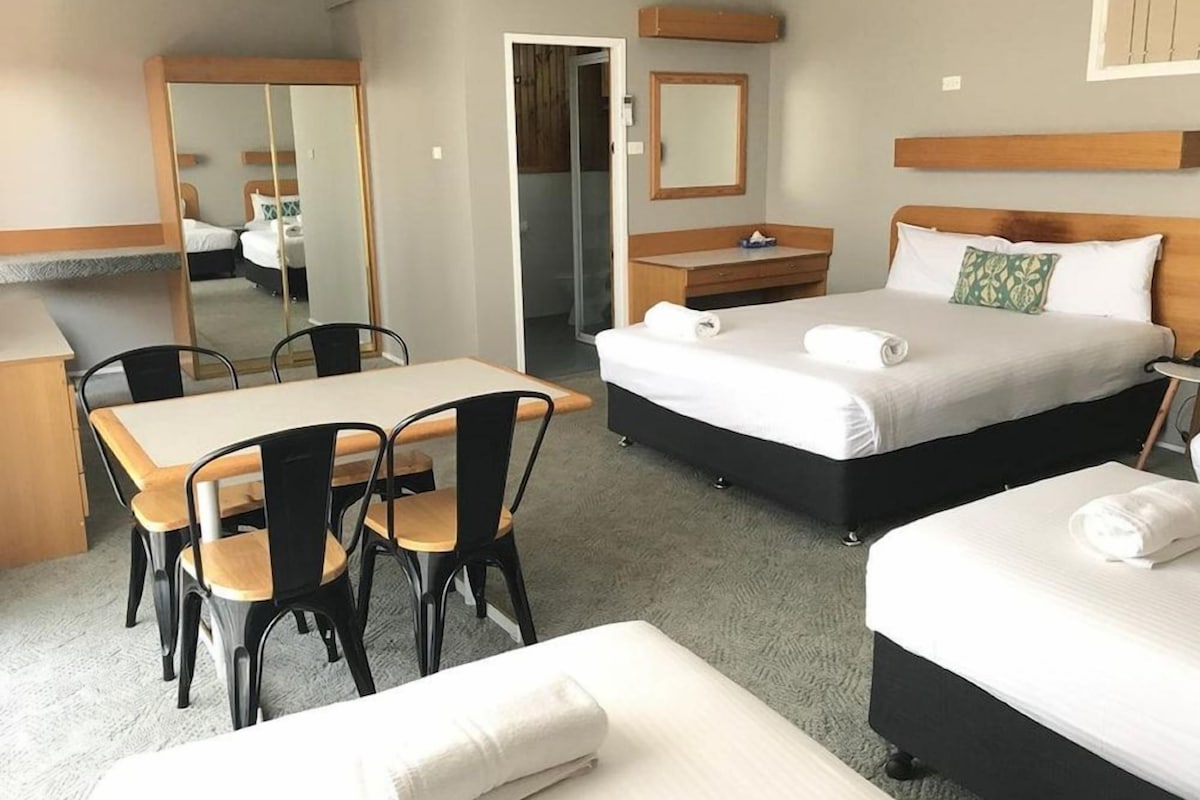 Ein Hotelzimmer mit Bett, Schreibtisch mit Stühlen, Spiegel, Kommode und separatem Schlafbereich.