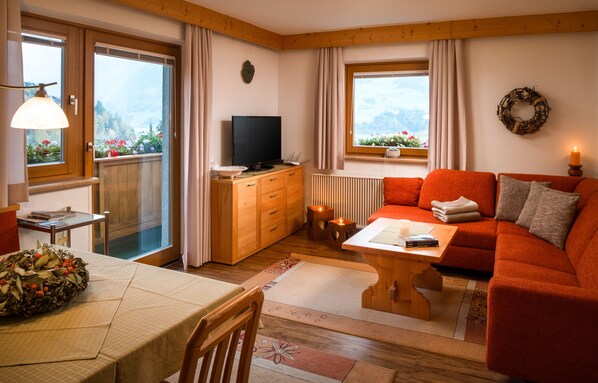 A cozy living room with a sofa, a TV, and a dining area with a table set for two.