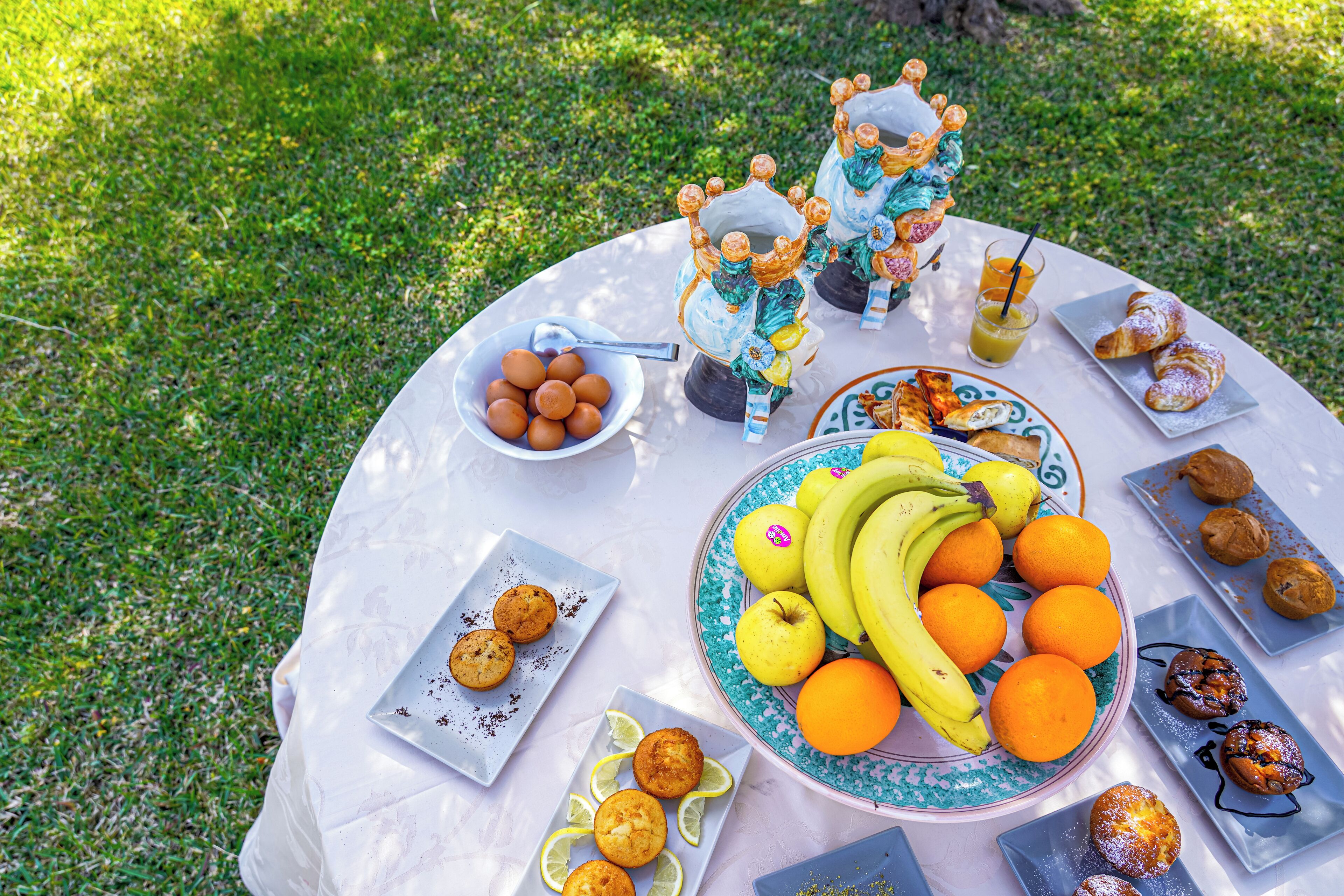 A round table with a variety of food items including fruits, pastries, and a decorative teapot.