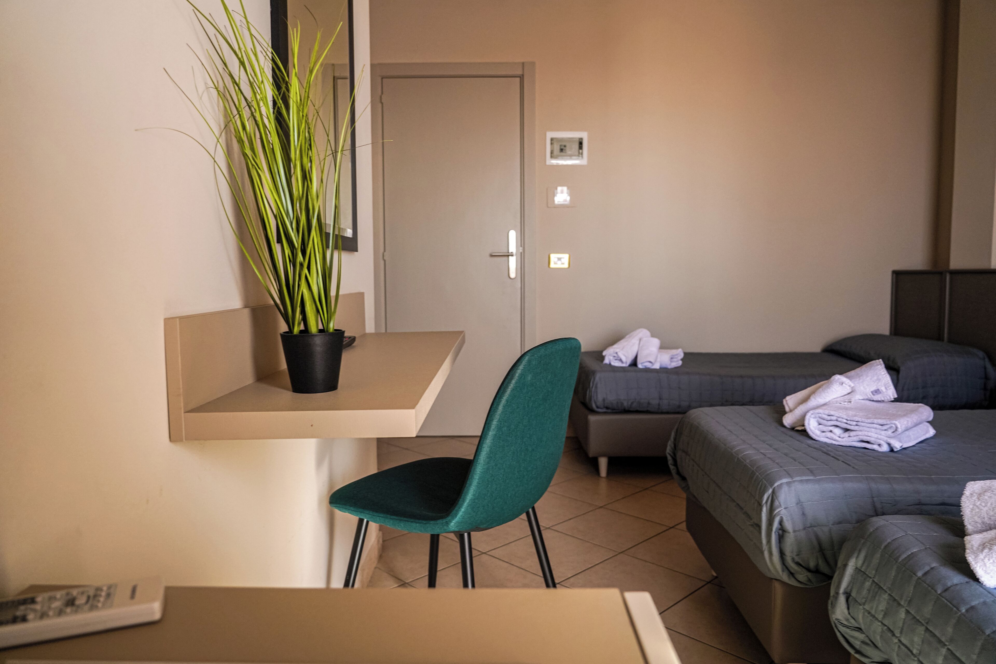 Habitación de hotel con escritorio, silla, dos camas y una planta en maceta.