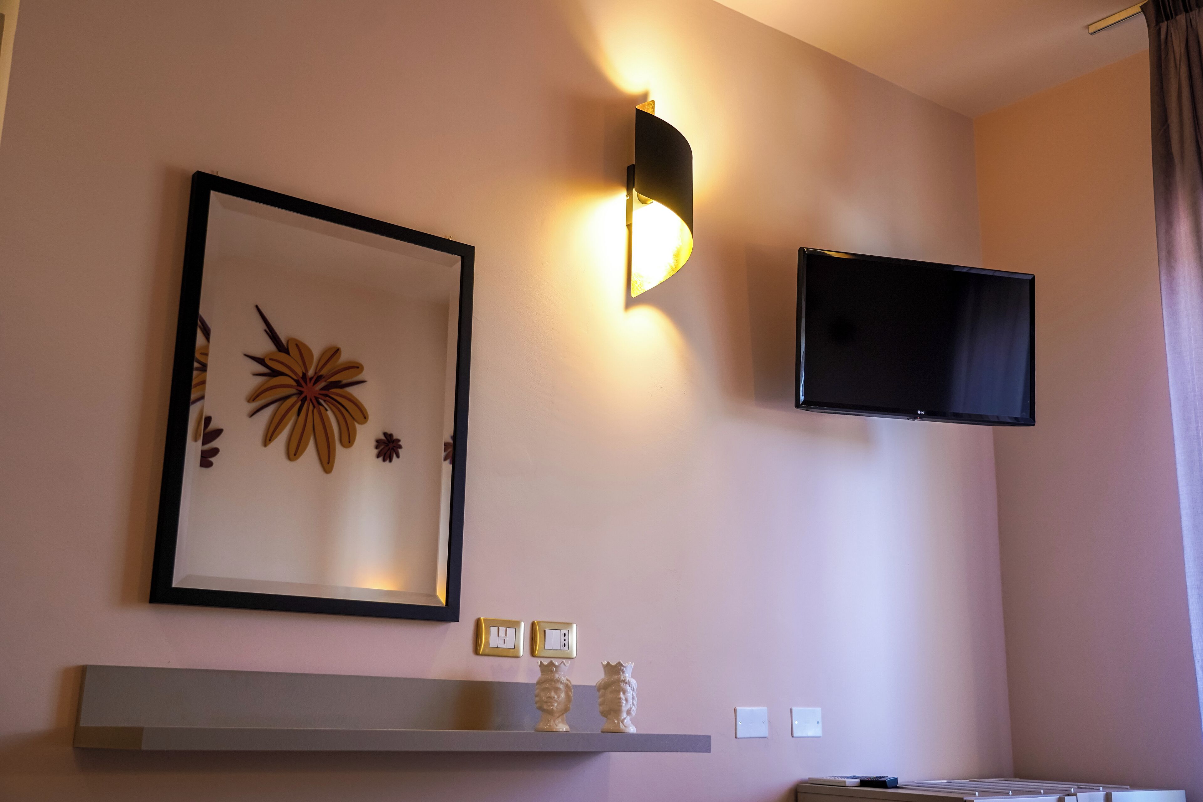 A wall-mounted TV and framed artwork above a shelf with decorative items.