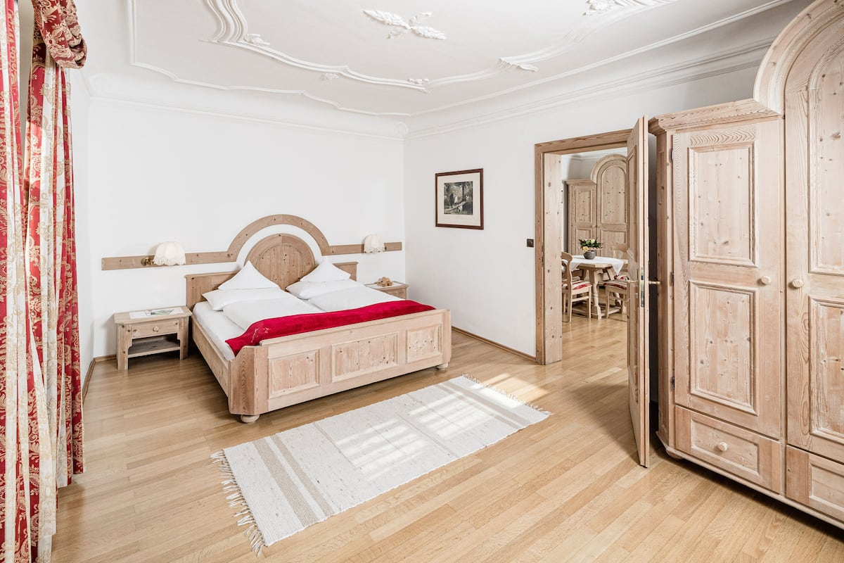 A bedroom with a wooden bed, a nightstand, a wardrobe, and a door leading to another room.