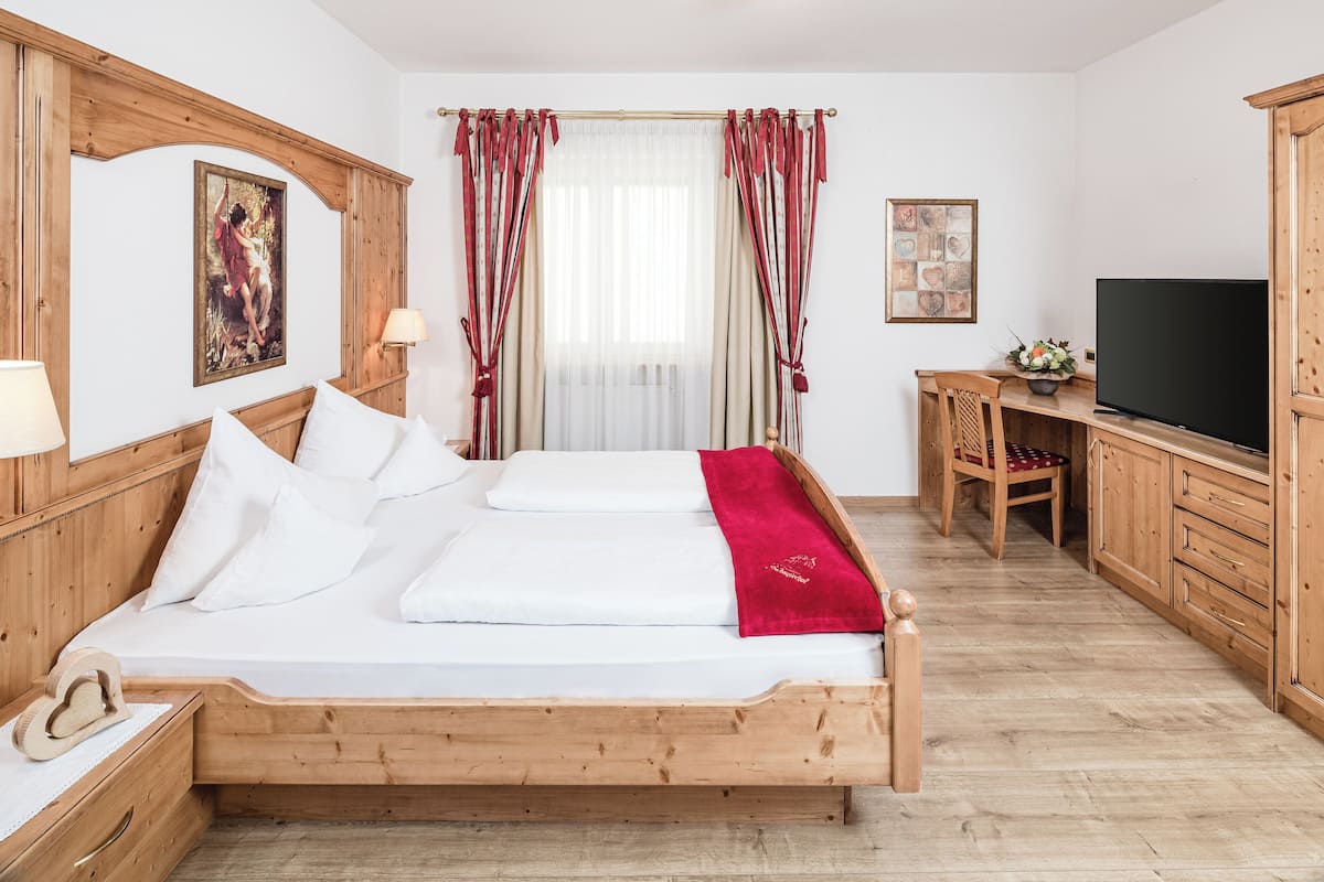 A wooden bed with white linens, a television, and a desk with a chair in a room with wooden floors and walls.