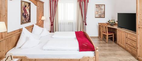 A wooden bed with white linens, a television, and a desk with a chair in a room with wooden floors and walls.
