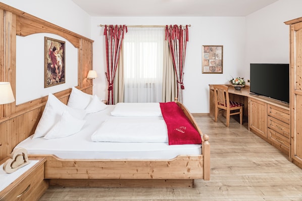 A wooden bed with white linens, a television, and a desk with a chair in a room with wooden floors and walls.