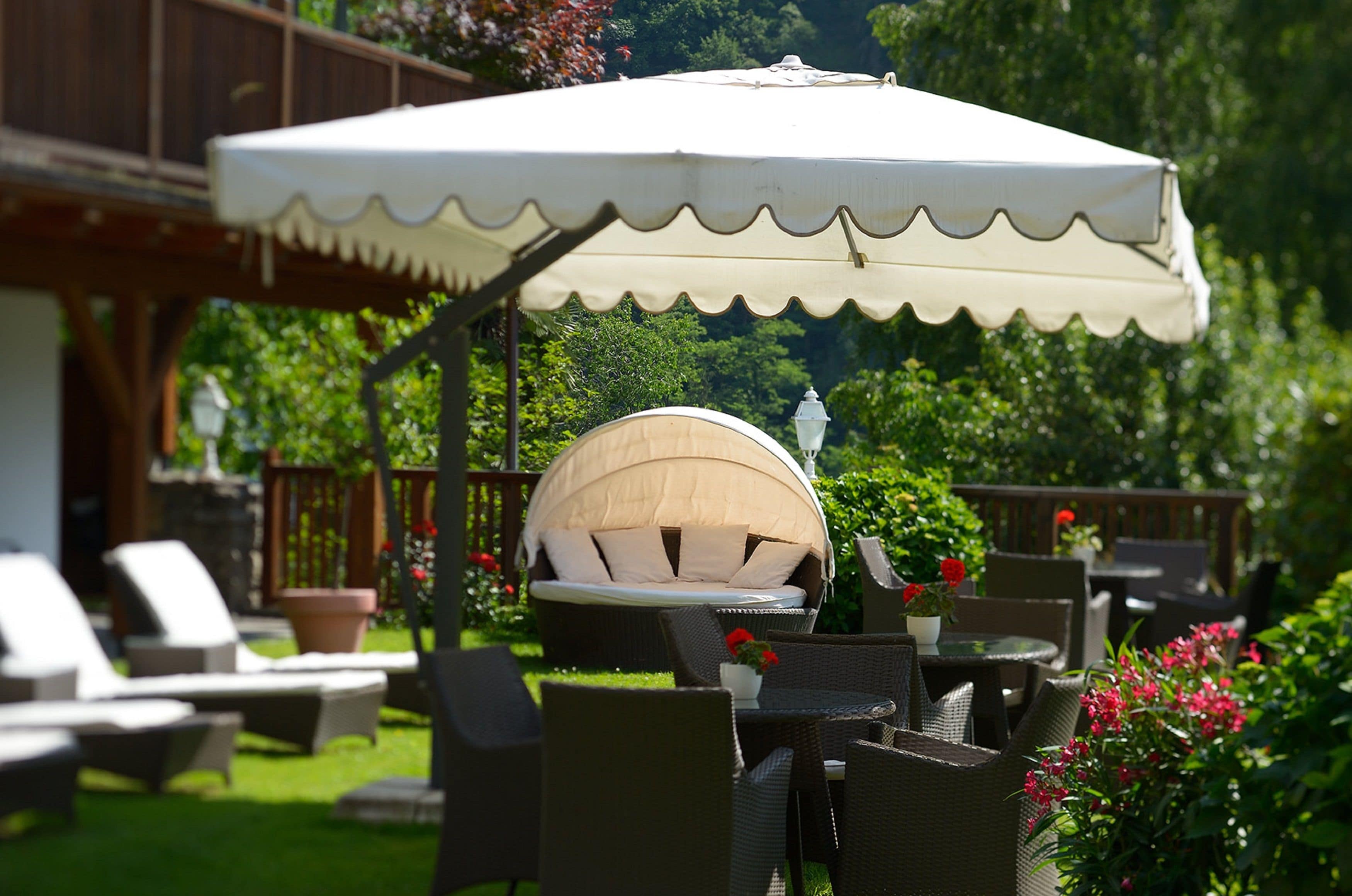 Ein Sitzbereich im Freien mit Korbmöbeln, ein überdachter Ruhebereich und ein Garten im Hintergrund.