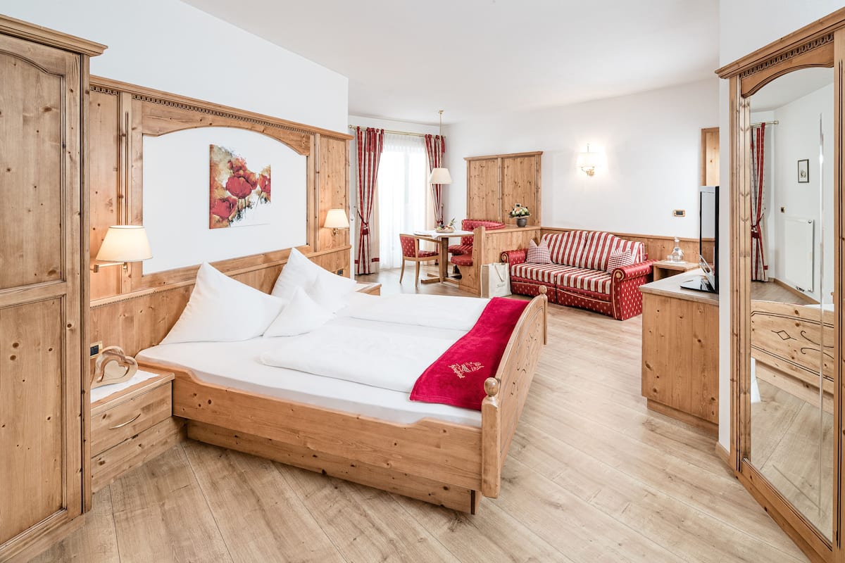 A wooden bed with white linens, a red and white striped sofa, and a dining table with chairs in a room with wooden floors and walls.