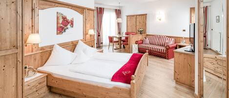 A wooden bed with white linens, a red and white striped sofa, and a dining table with chairs in a room with wooden floors and walls.