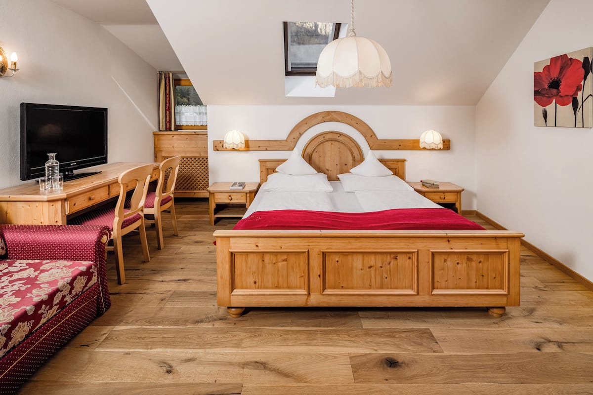 A bedroom with a wooden bed, a TV, a desk, and a chair.