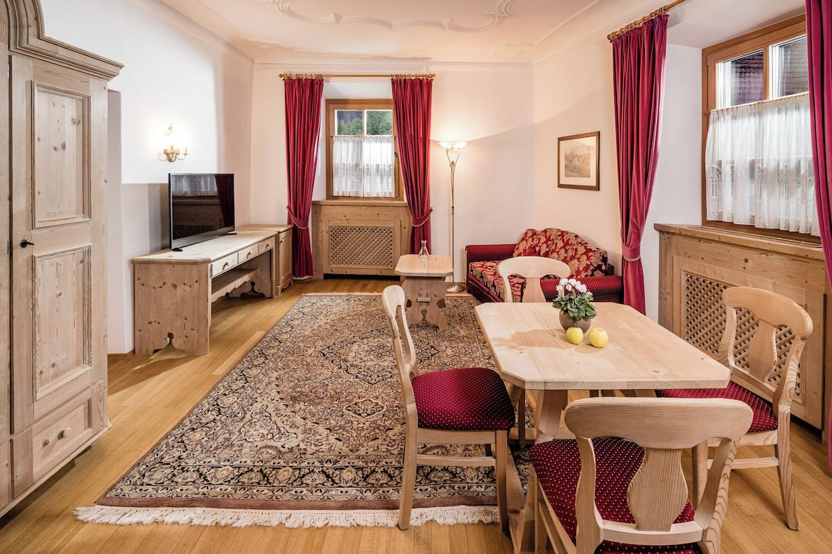 A room with a wooden table, chairs, a sofa, a TV, and a patterned rug.