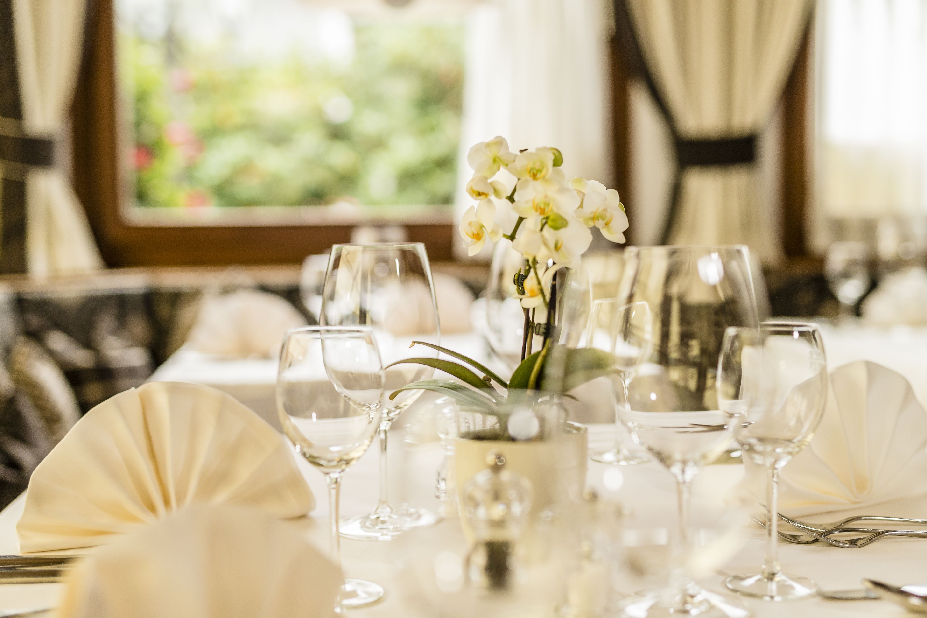 A table set for a formal dining occasion with white tablecloth, glassware, and a vase with white flowers.
