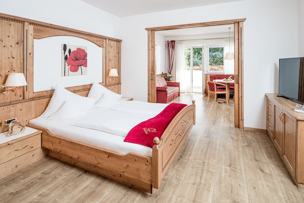 A wooden bed with white linens, a bedside table with a lamp, a red throw blanket, and a wooden headboard.