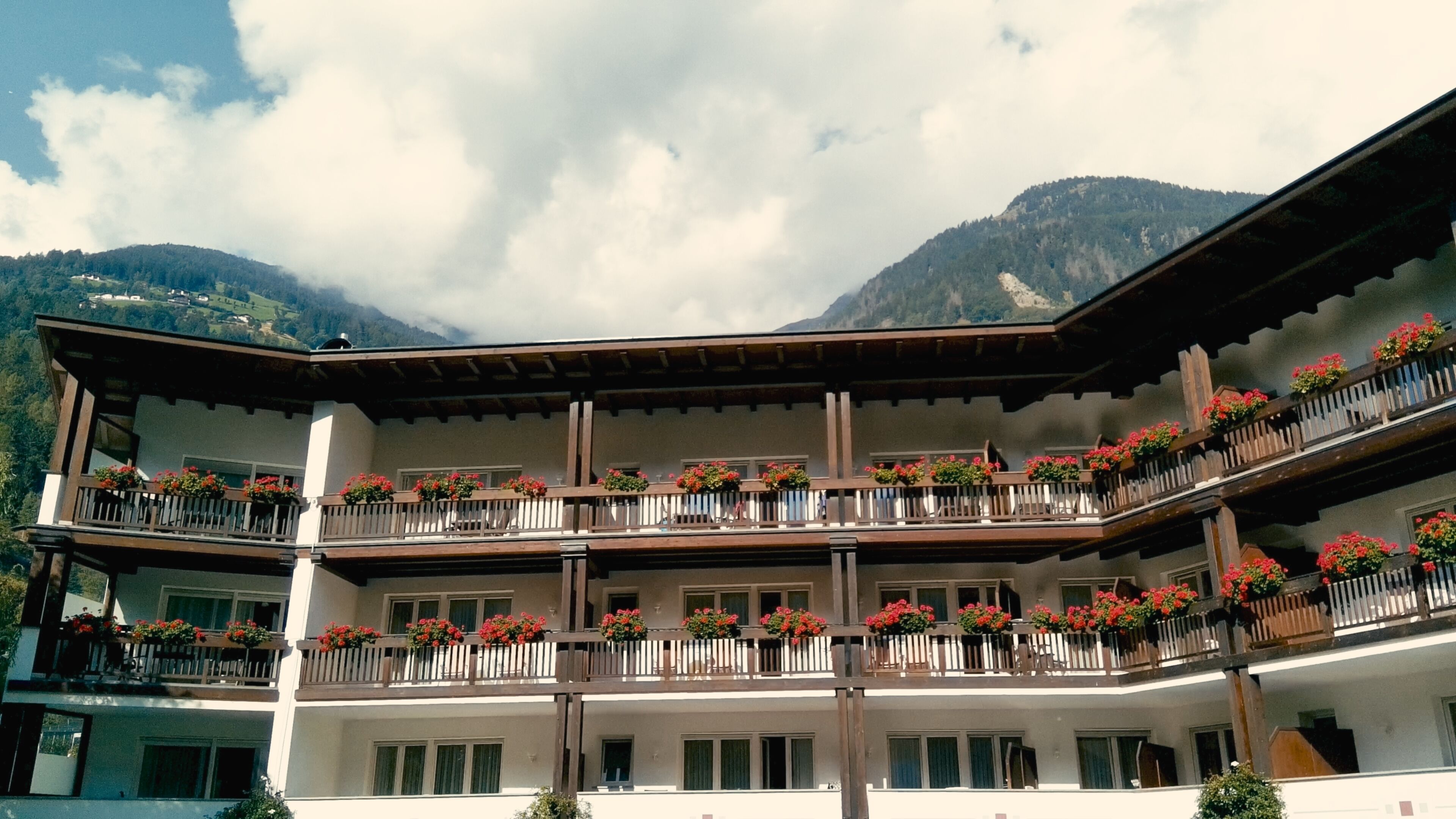 A multi-story hotel with balconies adorned with flower boxes, set against a mountainous backdrop.