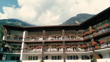 Un hotel a più piani con balconi decorati da fioriere, sullo sfondo di montagne.