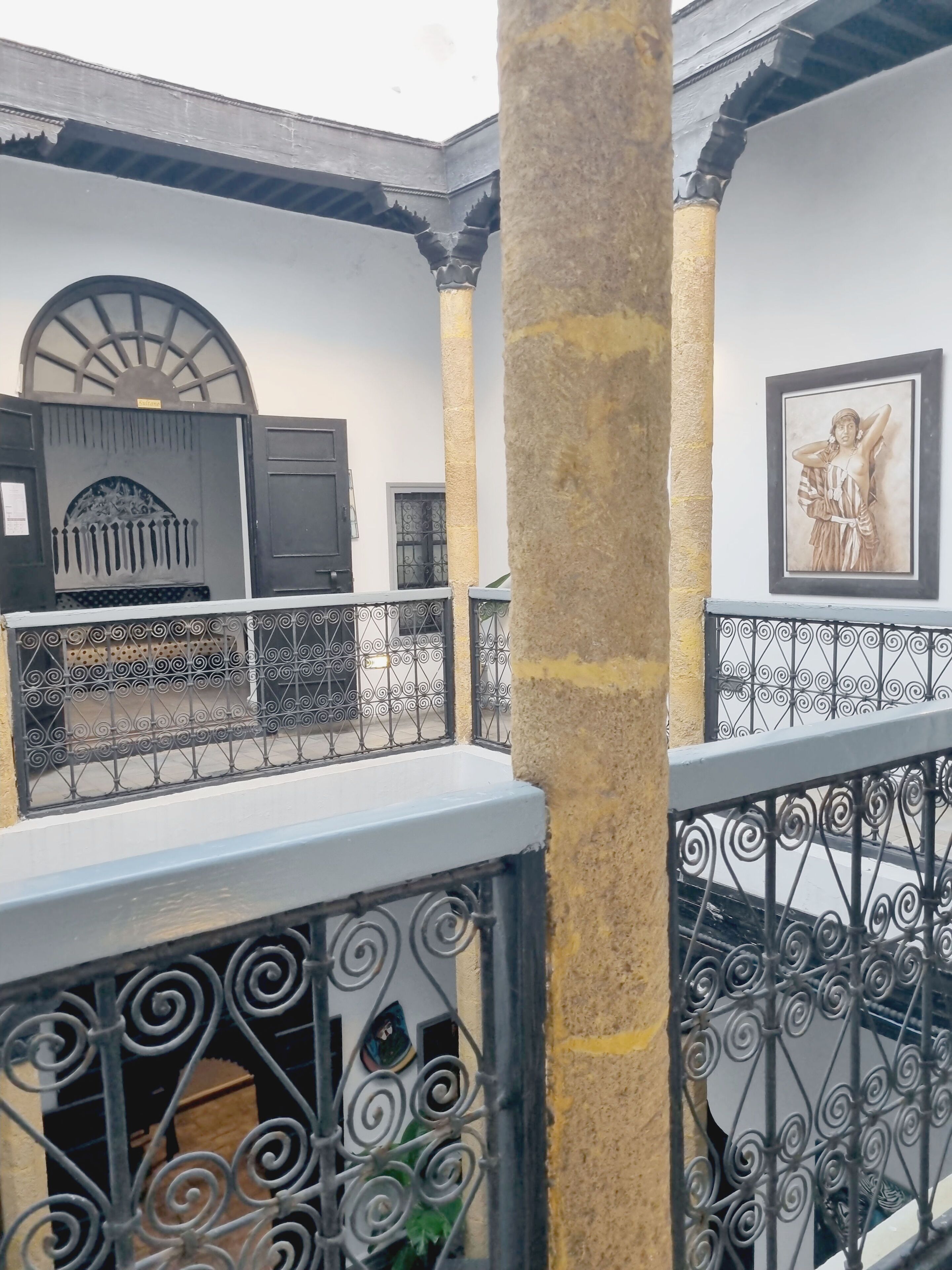 Un cortile con un balcone, ringhiere in ferro battuto, una colonna in pietra e un'opera d'arte incorniciata sulla parete.