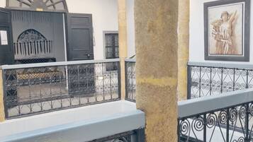 Un cortile con un balcone, ringhiere in ferro battuto, una colonna in pietra e un'opera d'arte incorniciata sulla parete.