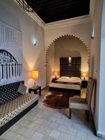 Un dormitorio con cama, sofá, sillón, pared con estampado y ventilador de techo.