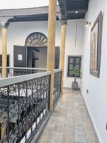 Un pasillo con suelo de baldosas, baranda de metal, una planta en maceta y una puerta con ventanal.