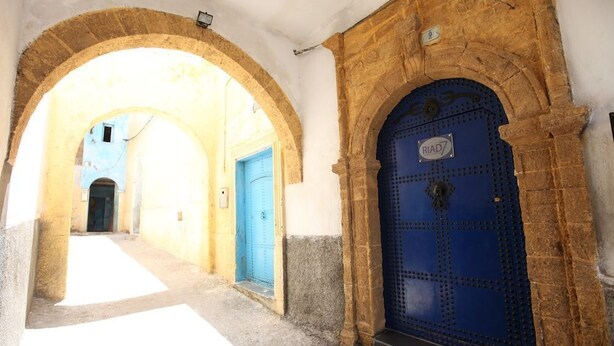 A narrow alleyway with a blue door and a stone archway.