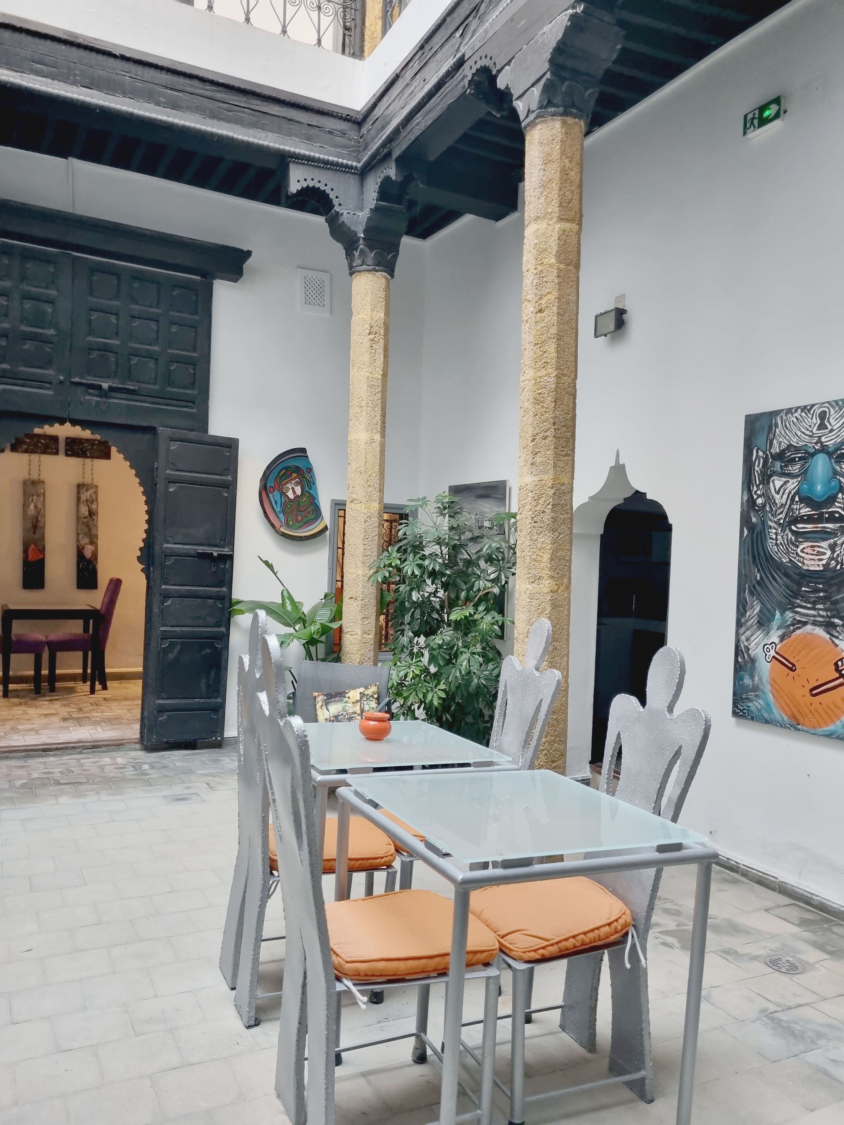 Une cour avec une table et des chaises, une porte et un mur orné d’œuvres d’art.