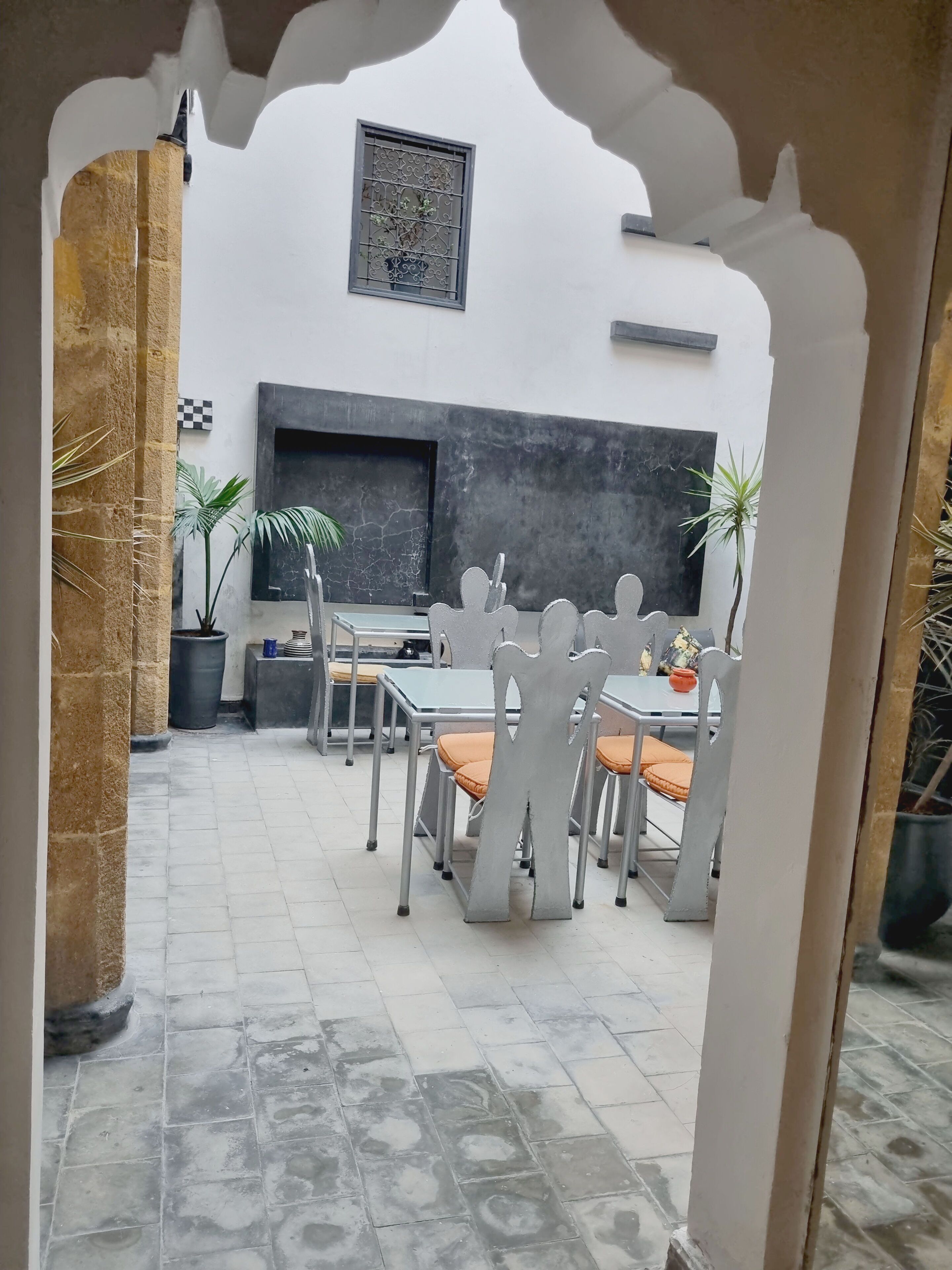 An outdoor dining area with a table and chairs, potted plants, and a wall-mounted TV.