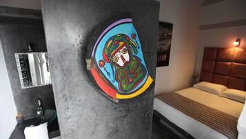 Une chambre d’hôtel moderne avec un grand lit, une salle de bain dotée d’un lavabo en verre et une œuvre d’art colorée accrochée au mur.