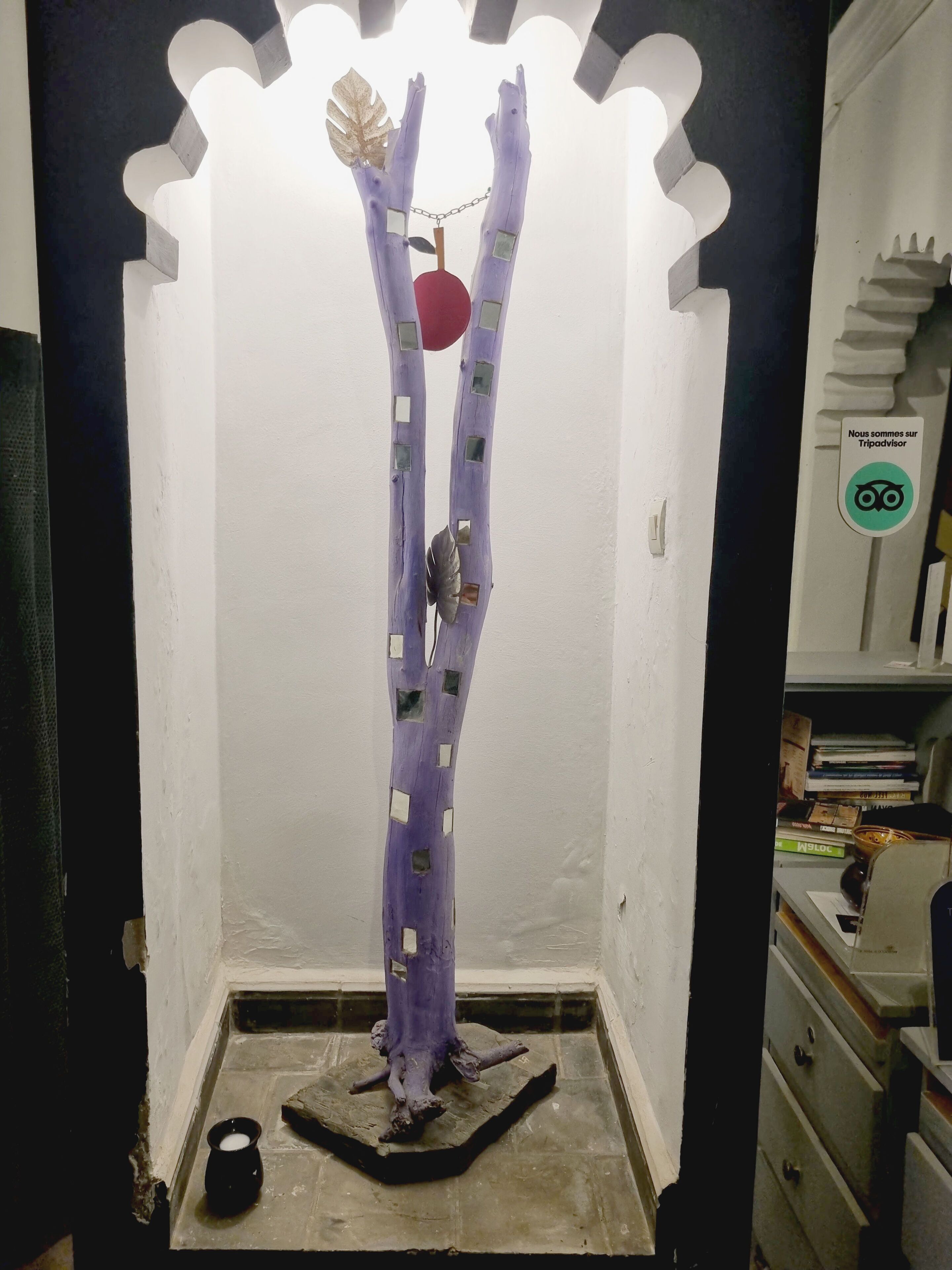 A room with a unique purple sculpture, a small black bowl, and a staircase with a sign in French.