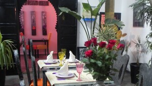 A dining area with a glass table, chairs, and a vase with red flowers.