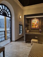 Un balcón amplio con vistas, una zona de estar con una mesa estampada y una pared decorativa con una obra de arte enmarcada.