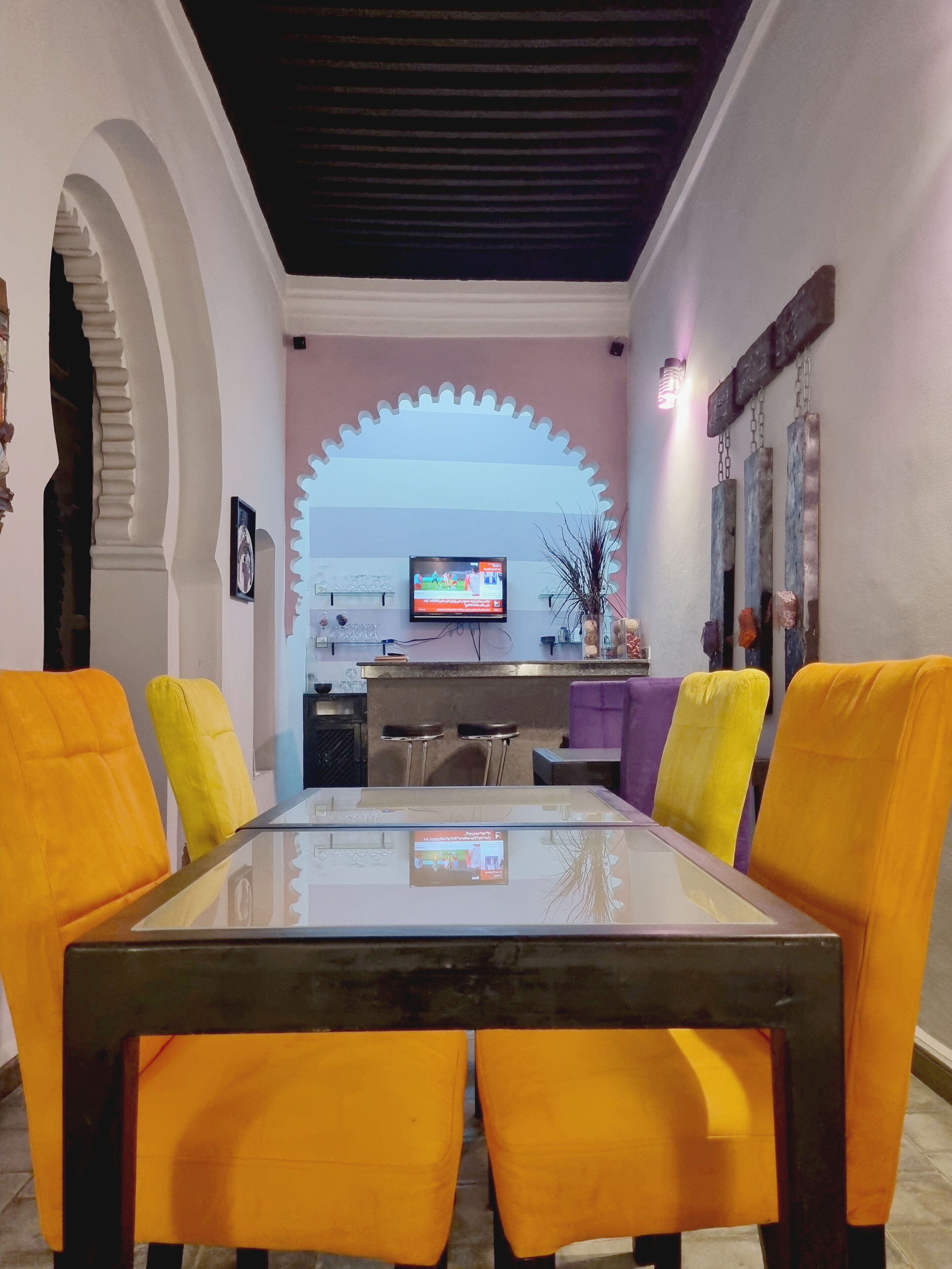 Zona pranzo con tavolo in vetro e quattro sedie, televisione montata a parete e un arco decorativo.