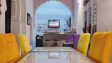 Zona pranzo con tavolo in vetro e quattro sedie, televisione montata a parete e un arco decorativo.