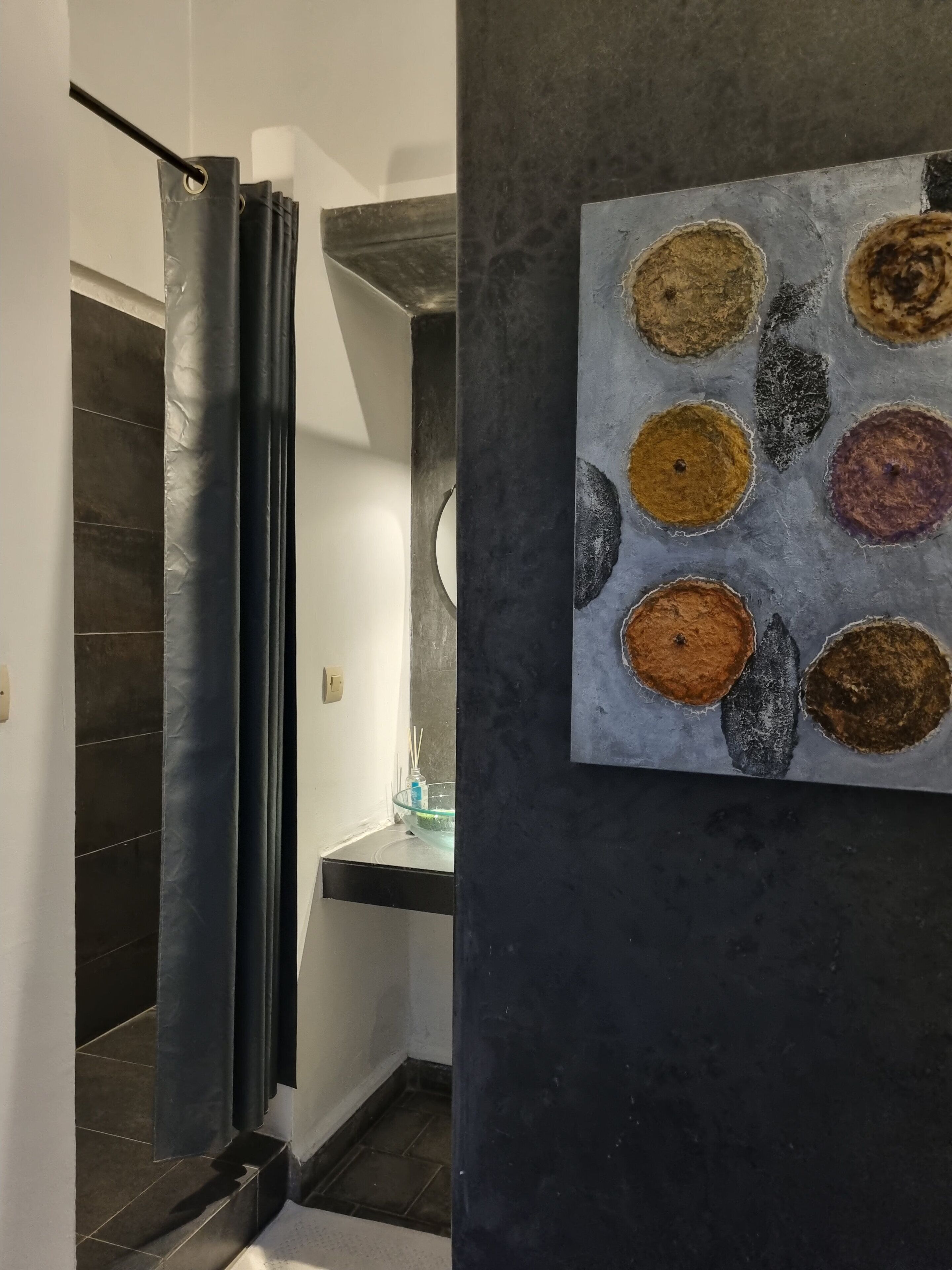 A modern bathroom with a shower curtain, a glass bowl on the sink, and a wall-mounted artwork.