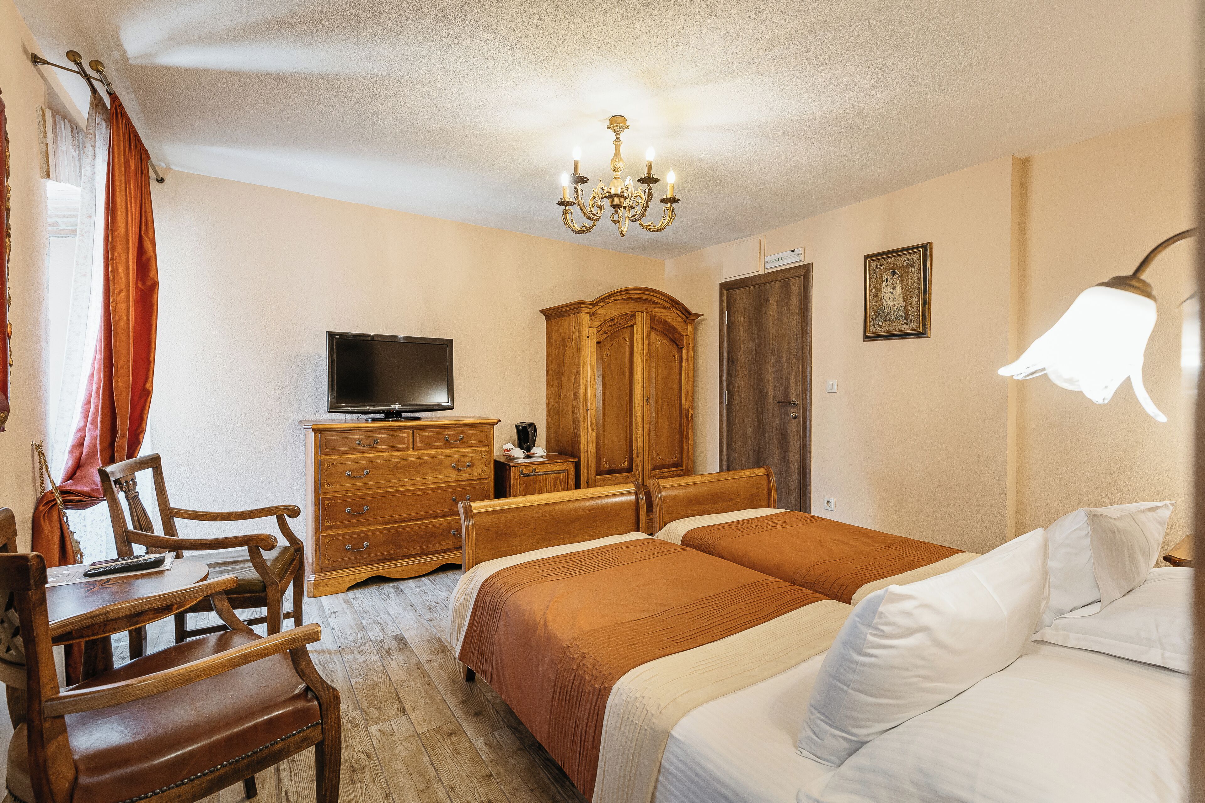 A bedroom with two beds, a wooden dresser, a television, and a chandelier.