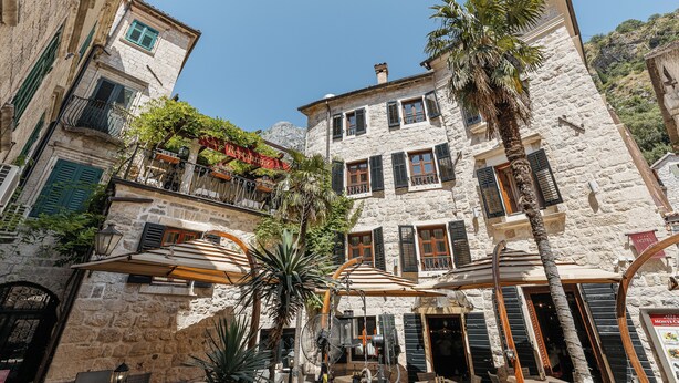 A stone building with balconies, outdoor seating, and a palm tree. - Hotel Monte Cristo (Kotor)
