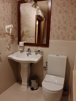 Un baño con lavamanos pedestal, inodoro, espejo y secador de pelo en la pared.